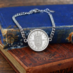 1956 shilling coin bracelet with a silver-coloured bezel and curb chain, English shield reverse, laid over two old hardback books