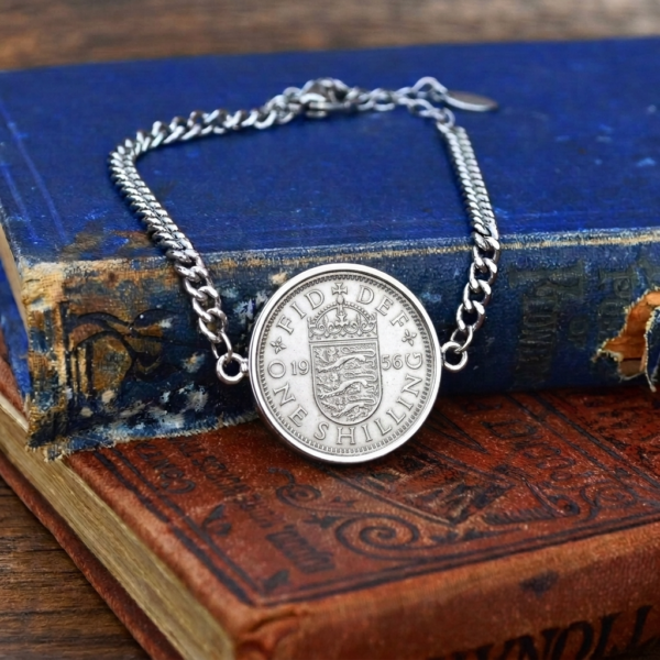 1956 shilling coin bracelet with a silver-coloured bezel and curb chain, English shield reverse, laid over two old hardback books
