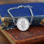 1958 one shilling coin in a silver-coloured bezel on a curb chain bracelet, English shield reverse, resting on old cloth-bound books