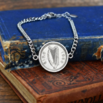 1960 Irish sixpence set in a silver-tone bracelet, harp side showing, resting on a worn blue cloth book