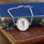 Harp side of a 1961 Irish sixpence framed in silver-tone on a curb chain bracelet, over two worn hardbacks
