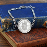 1962 one shilling coin bracelet on a silver-coloured curb chain, English shield side up, laid on worn blue and red books