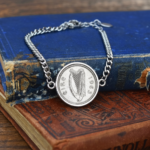 Silver-tone curb chain bracelet with a 1963 Irish sixpence, harp and eire side up, on old blue and red books