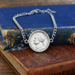 1965 US nickel in a silver-coloured bezel on a curb chain bracelet, resting on old blue and red cloth books
