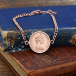 Rose gold-tone curb chain bracelet set with an Australian coin dated 1966, Queen Elizabeth II portrait, on worn antique books