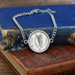 1966 Irish sixpence, harp and eire side up, in a silver-tone bezel on a curb chain bracelet, resting on old books