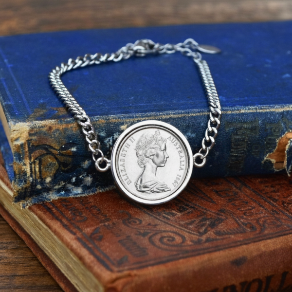 1967 Australian coin in a silver-tone bezel on a silver-tone curb chain bracelet, laid over worn blue and red antique books