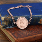 Rose gold-tone curb chain bracelet set with an Australian coin dated 1967, Queen Elizabeth II portrait, on worn antique books