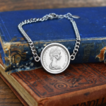 1968 Australian coin in a silver-tone bezel on a silver-tone curb chain bracelet, laid over worn blue and red antique books