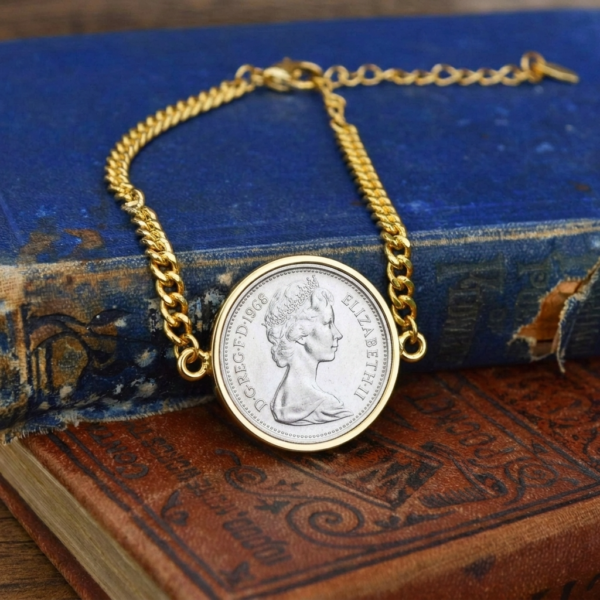 1968 coin with young Elizabeth II portrait in a gold-tone bezel on a gold curb chain bracelet, on a worn blue book