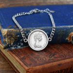 1969 Australian coin in a silver-tone bezel on a silver-tone curb chain bracelet, laid over worn blue and red antique books