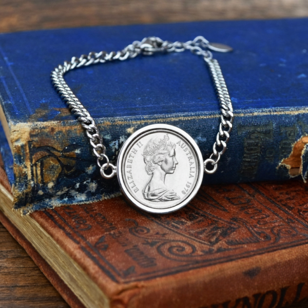 1970 Australian coin in a silver-tone bezel on a silver-tone curb chain bracelet, laid over worn blue and red antique books
