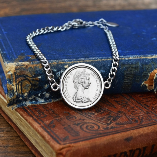 1971 Australian coin in a silver-tone bezel on a silver-tone curb chain bracelet, laid over worn blue and red antique books