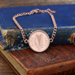 1971 Irish coin with harp and eire lettering set in a rose gold-tone bracelet, on worn blue and tan books