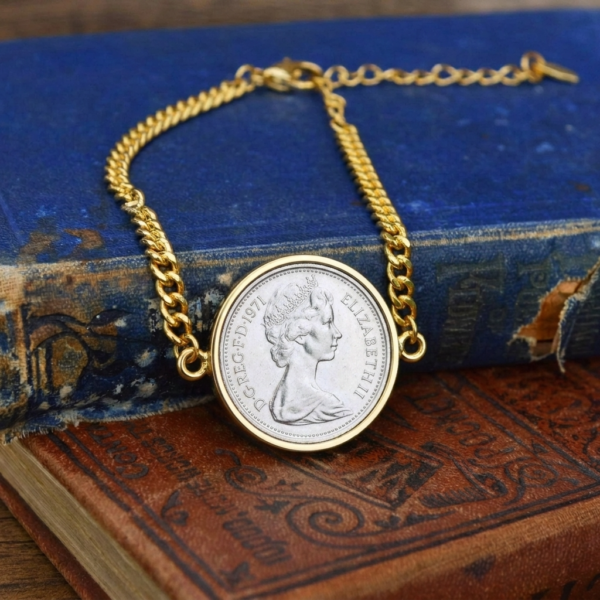 1971 coin with young Elizabeth II portrait in a gold-tone bezel on a gold curb chain bracelet, on a worn blue book