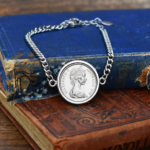 1972 Australian coin in a silver-tone bezel on a silver-tone curb chain bracelet, laid over worn blue and red antique books