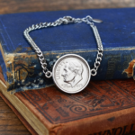 1973 US dime in a silver-coloured bezel on a curb chain bracelet, resting on a worn blue hardback book