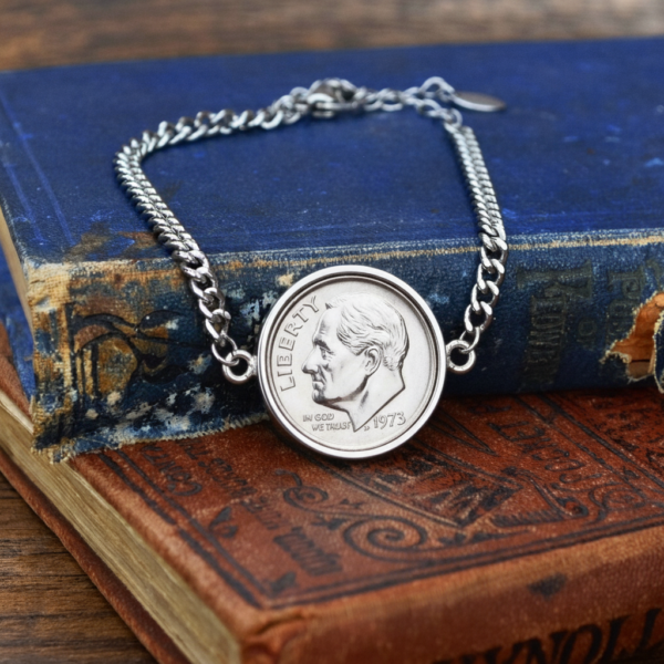 1973 US dime in a silver-coloured bezel on a curb chain bracelet, resting on a worn blue hardback book
