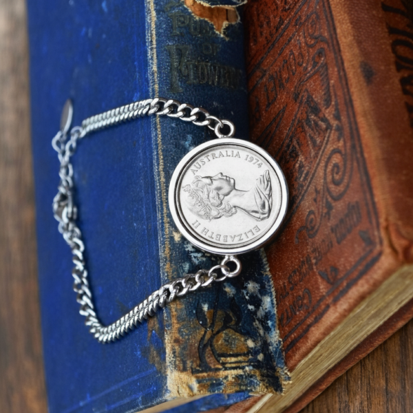 1974 Australian coin in a silver-tone bezel on a curb chain bracelet, laid open across the spines of two worn books