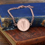1974 Irish coin with harp and eire lettering set in a rose gold-tone bracelet, on worn blue and tan books