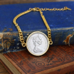 1975 coin with young Elizabeth II portrait in a gold-tone bezel on a gold curb chain bracelet, on a worn blue book