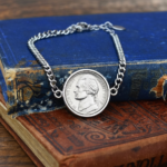 1975 US nickel set in a silver-coloured bezel on a curb chain bracelet, resting on worn blue and brown books