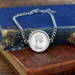1978 Australian coin in a silver-tone bezel on a curb chain bracelet, young Elizabeth II portrait, resting on old books