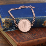 1978 Irish coin with harp and eire lettering set in a rose gold-tone bracelet, on worn blue and tan books