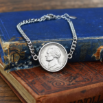 Silver-coloured curb chain bracelet with a 1978 US nickel in a round bezel, laid over old hardback books