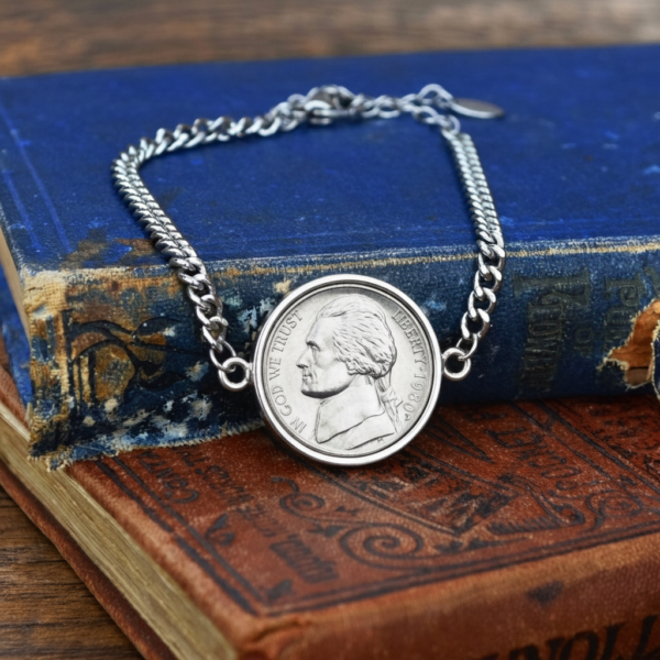 1980 US five cent coin in a silver-coloured bezel on a chain bracelet, propped on a faded blue hardback
