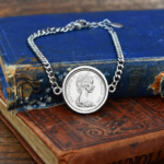 1984 Australian coin in a silver-tone bezel on a curb chain bracelet, young Elizabeth II portrait, on faded blue and red books