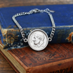 1984 USA Roosevelt dime set in polished silver on a curb chain bracelet, resting on a worn blue cloth book