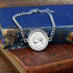 1984 US five cent coin in a silver-coloured bezel on a chain bracelet, propped on a faded blue hardback