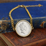 1985 old five pence coin in a gold-coloured bezel on a curb chain bracelet, laid across worn blue and red hardback books
