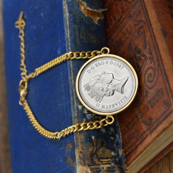 1987 old five pence coin in a gold-coloured bezel on a curb chain bracelet, laid across worn blue and red hardback books