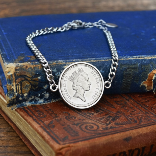 1987 old five pence coin in a silver coloured bracelet, crowned Elizabeth II head, on worn blue and brown books