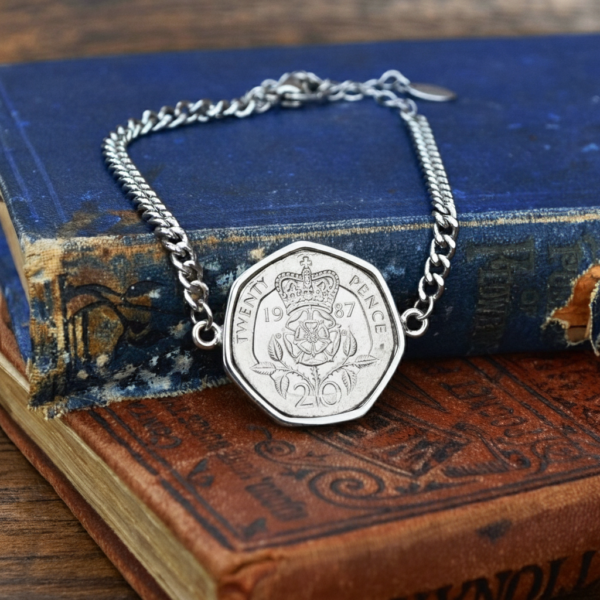 1987 twenty pence coin set in a silver-coloured bracelet, crowned Tudor rose facing up, resting on old hardback books