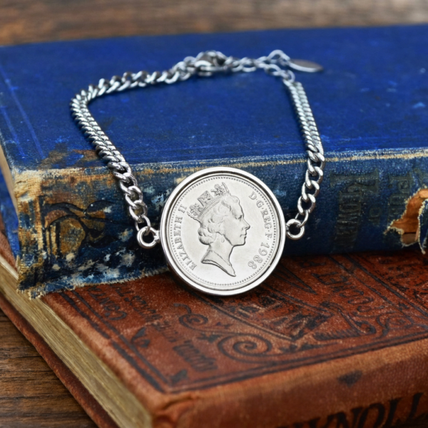 1988 old five pence coin in a silver coloured bracelet, crowned Elizabeth II head, on worn blue and brown books