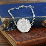 1989 twenty pence in a silver-coloured bezel on a chain bracelet, lying on the corner of a faded blue hardback book