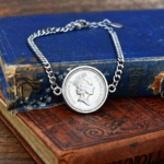 1991 coin with the crowned Queen Elizabeth II portrait in a silver-tone bezel on a curb chain bracelet, on old books