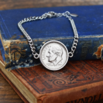 1991 US dime in a silver-coloured bezel on a curb chain bracelet, resting on worn antique books