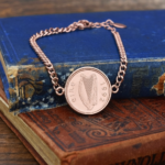 1992 Irish harp coin set in a rose gold bezel on a curb chain bracelet, shown on worn blue and red cloth books