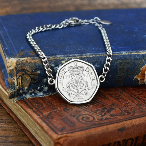 1993 twenty pence in a silver-coloured bezel on a chain bracelet, lying on the corner of a faded blue hardback book