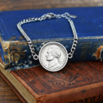 Silver-coloured bracelet holding a 1994 US five cent nickel, resting on a faded blue hardback book