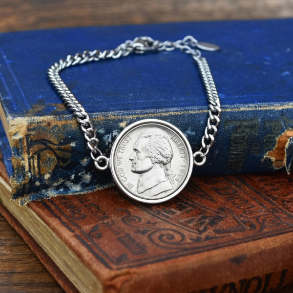 Silver-coloured bracelet holding a 1994 US five cent nickel, resting on a faded blue hardback book