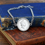 1995 coin, crowned Queen Elizabeth II portrait, set in a silver-tone bezel on a curb chain bracelet over antique books