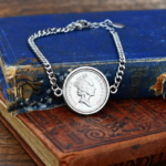 1997 coin with the crowned Queen Elizabeth II portrait in a silver-tone bezel on a curb chain bracelet, on old books