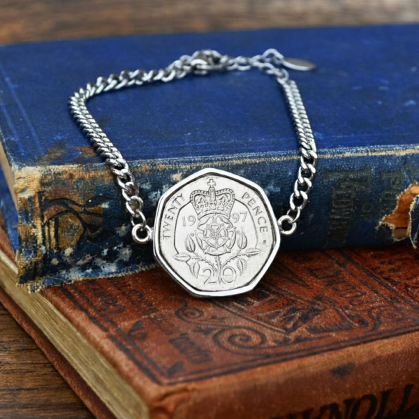 1997 twenty pence in a silver-coloured bezel on a chain bracelet, lying on the corner of a faded blue hardback book