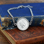 Silver-tone curb chain bracelet set with a 1999 coin, Queen Elizabeth II portrait side up, resting on a faded blue book