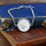 2000 coin showing the Queen Elizabeth II portrait in a round silver-tone bezel on a curb chain bracelet, on worn old books